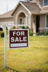 Close-up of a real estate for sale sign hanging in front of a beige residential home with arched doorway and clean lawn.
