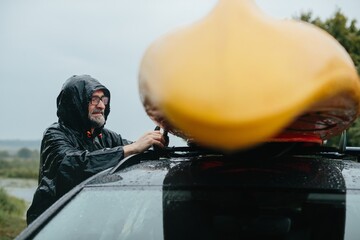 Senior man preparing kayak on car roof during rain