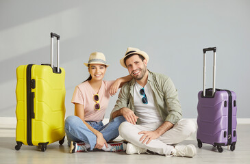 Portrait of happy smiling young couple sitting with suitcases on gray studio background and looking...