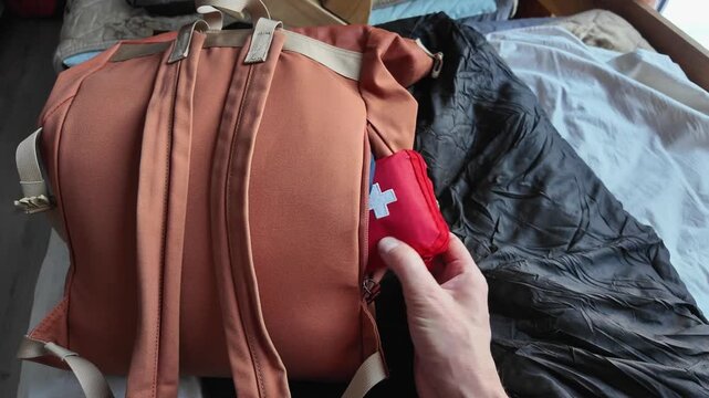 First Aid Stored, Hand Secures Medical Kit In Backpack, Arranged Emergency Supplies For Easy Outdoor Access, Securely Packed First Aid Essentials In Backpack For Immediate Use During Excursions
