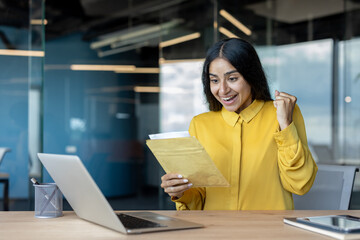 A happy young businesswoman is sitting at her office desk and is happy about the letter she received