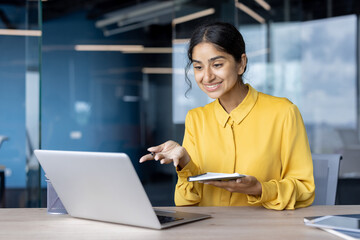 Young Indian businesswoman holding an online meeting, talking on a laptop and using a notepad
