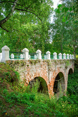 old, weathered brick arched bridge in the forest. Ancient worn bridge with exposed red bricks. For historical articles about hidden European landmarks and ancient infrastructure