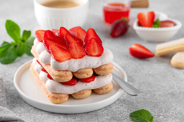 Strawberry tiramisu. Italian layered dessert with mascarpone cream and biscuits on a plate with cup of coffee on a concrete background.