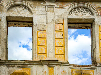 Ancient facade with two ornate window frames. Sky through the window. Hope, renewal concept. Historical abandoned structure. for articles on urban decay, architectural restoration.
