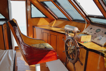 Boat wheelhouse shows a steering wheel, seat, and control panel during daytime at a marina © Karabas