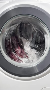 Front-loading washing machine in operation with rotating drum during an active wash cycle. Water and