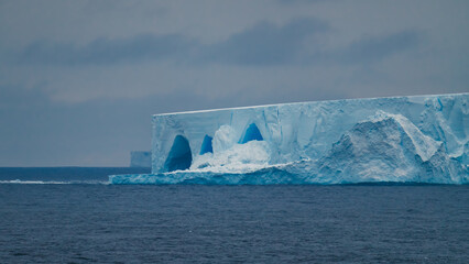 Iceberg in Antarctica. Beautiful Gigantic Formation of Ice. Blue and White Color Flat Top with Rigid Edges Caverns. Melting Icecaps Climate Change © And They Travel