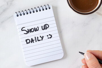 Show up daily, inspirational handwritten quote in notebook with coffee cup. Top view. The concept of personal growth, motivation, progress, and success.