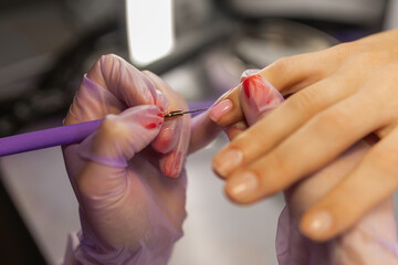 Close up of professional manicure process. Nail technician applying gel polish on female nails with brush while wearing protective gloves in beauty salon