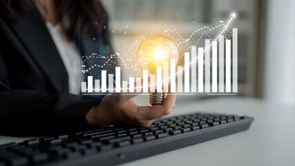 A business professional holds a light bulb over a keyboard, symbolizing innovation and creativity, while analyzing financial growth trends on a virtual screen. Impute