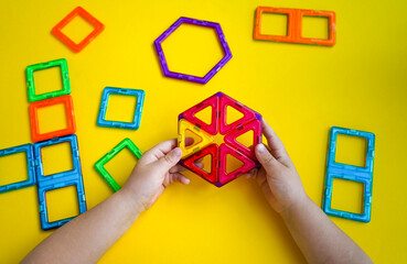 A young builder assembles colorful magnetic pieces of different geometric configurations into imaginative structures during play.