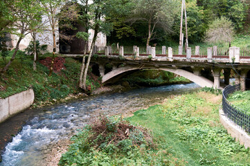 Small railway bridge spans river, its metal structure contrasting with natural water flow and surroundings.