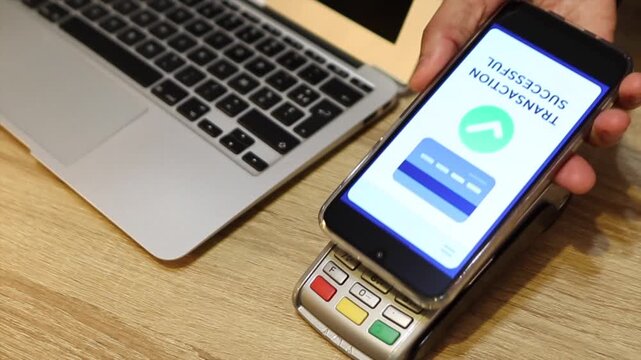 Customer making a secure wireless payment by holding a smartphone over a pos terminal. The screen shows a successful transaction confirmation