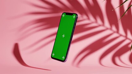 Modern smartphone with green screen floating and rotating on pink background with palm leaf shadows. Concept of digital marketing