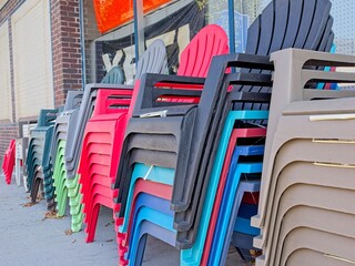 Stacks of colorful plastic Adirondack chairs line up on sidewalk