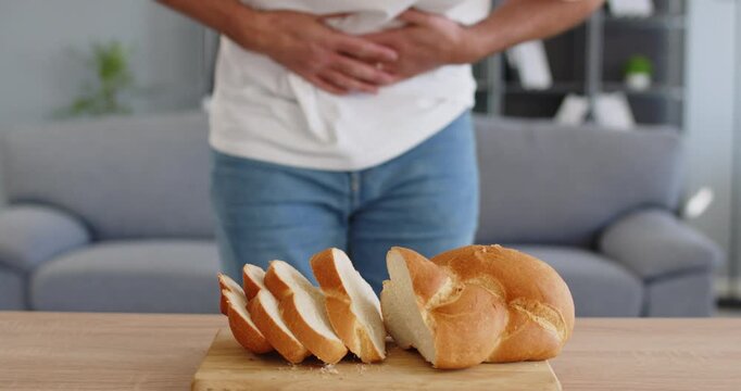 Gluten bread intolerance man stomach pain celiac. Loaf on board at home, showing digestive pain from wheat, diarrhea or chronic constipation. Gluten intolerance and abdominal pain concept.