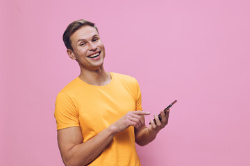 smiling man using smartphone in yellow tshirt pointing finger on digital device isolated on pink background cyber security concept