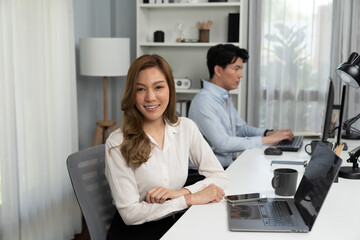 Profile smiling beautiful Asian businesswoman looking camera to portrait pose at modern office on working desk casual day. Blurry background man colleague analyzing data market plan on pc. Infobahn.