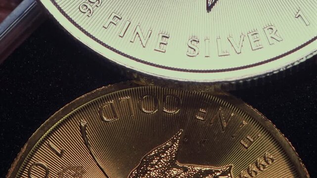 Close-up of the inscription &ldquo;fine silver&rdquo; on a silver coin lying on a gold coin labeled &ldquo;fine gold,&rdquo; representing precious metal prices and the gold-to-silver ratio.