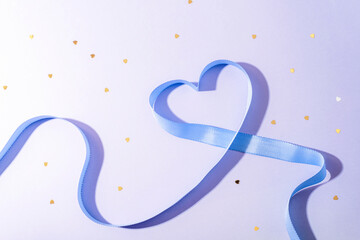 Blue ribbon shaped as heart on light pastel background with small golden confetti. Valentines day concept