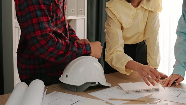 Smart architect and safety engineer discussion about building blueprint on table with architectural document, measurement tools and wooden block scatter around at modern office. Closeup. Delineation.