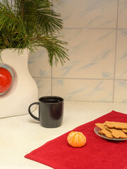 black mug with a drink against a vase with pine branches