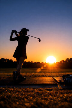 Young junior golfer practicing in a driving range with beautiful sunset light in winter.
