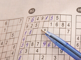 Close up of blue pen pointing at numbers in partially completed sudoku logical puzzle grid