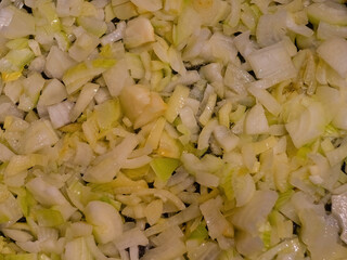 Fresh chopped onion pieces with glossy texture on wooden surface, top view of diced white onion ready for cooking, culinary ingredient for recipes and food preparation background.
