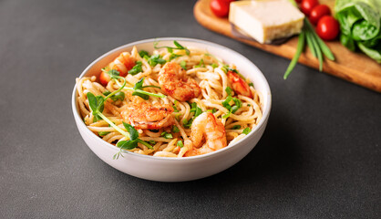 Spaghetti with cream sauce, parmesan, shrimps and onion, decorated with pea micro greens in white ceramic bowl on black stone background close up. 