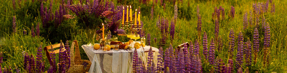 Banner. Beautiful romantic outdoor wedding decor. Table decorated with purple lupines flowers, lemons. Wineglasses with limoncello. Sunset, summer, golden hour. Perfect surprise date for loving couple