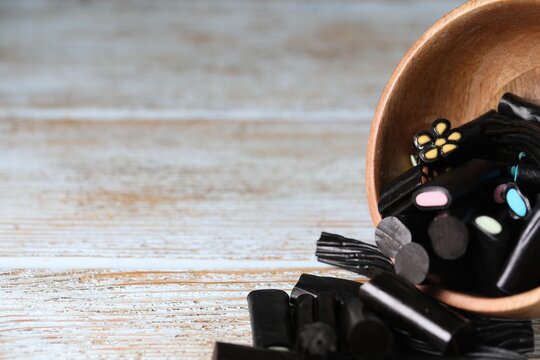 Natural licorice candies in bowl on wooden table, closeup. Space for text