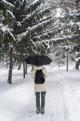 Person wearing a light jacket walking with an open black umbrella on a snowy trail, emphasizing cold weather and mobility