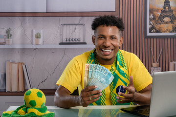 Brazilian fan happily holding money while using a laptop.