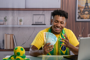 Brazilian fan happily holding money while using a laptop.
