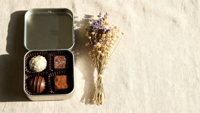サステナブルなバレンタインギフトのヴィーガンチョコレートとドライフラワーを自然素材の上に並べたミニマルフラットレイ、広告用コピースペース背景-生成AI