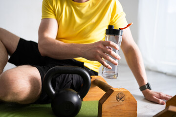 Sporty Man Relaxing After Morning Sport Routine By Sitting On The Floor At Home And Drinking Water