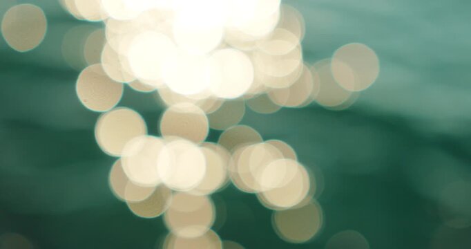 Glowing white bokeh highlights float on emerald sea water in motion