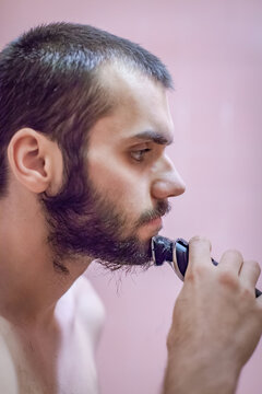 Close-up side view of a shirtless Man shaving his beard with an electric shaver