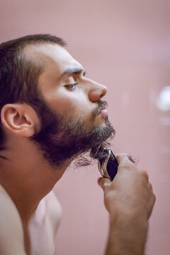 Close-up side view of a shirtless Man shaving his beard with an electric shaver