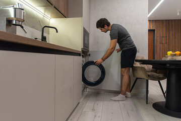 Man loading laundry into front-load washing machine at home