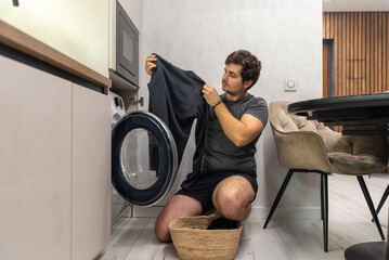 Young man taking clothes out of washing machine at home