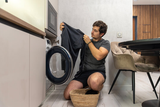 Young man taking clothes out of washing machine at home - Powered by Adobe