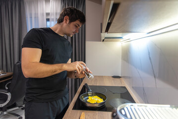 Man seasoning fried eggs with grinder in modern minimalist kitchen