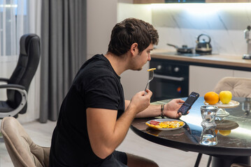 Man multitasking with smartphone while eating breakfast at kitchen table