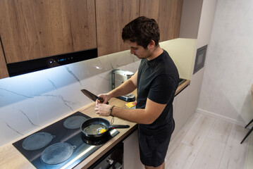 Man cracking egg into pan on induction cooktop in modern kitchen