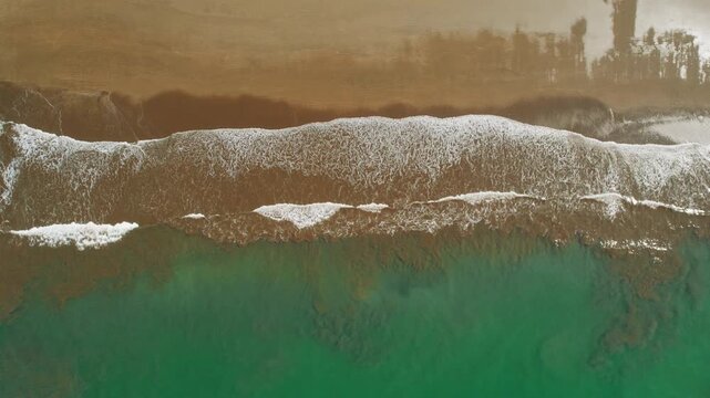 Ocean waves meeting dark smooth sandy shore forming white foam patterns in sunlight
