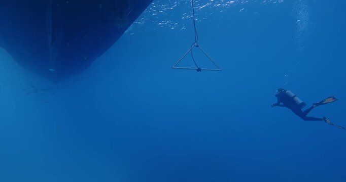 Scuba diver at safety stop by boat trapeze.