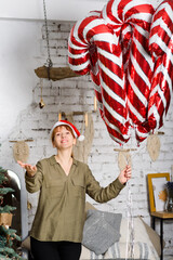 A smiling woman in a Santa hat holds a bunch of large candy cane-shaped foil balloons.